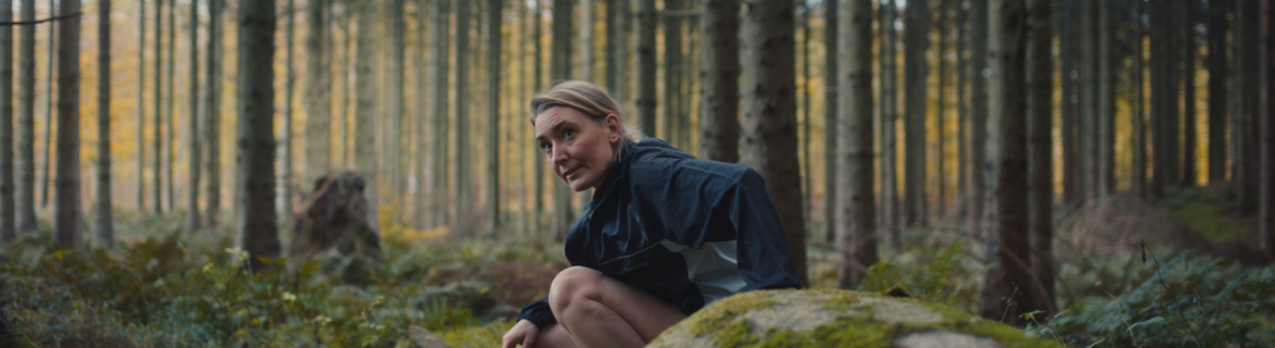 Kvinna som sitter bakom en sten i skogen